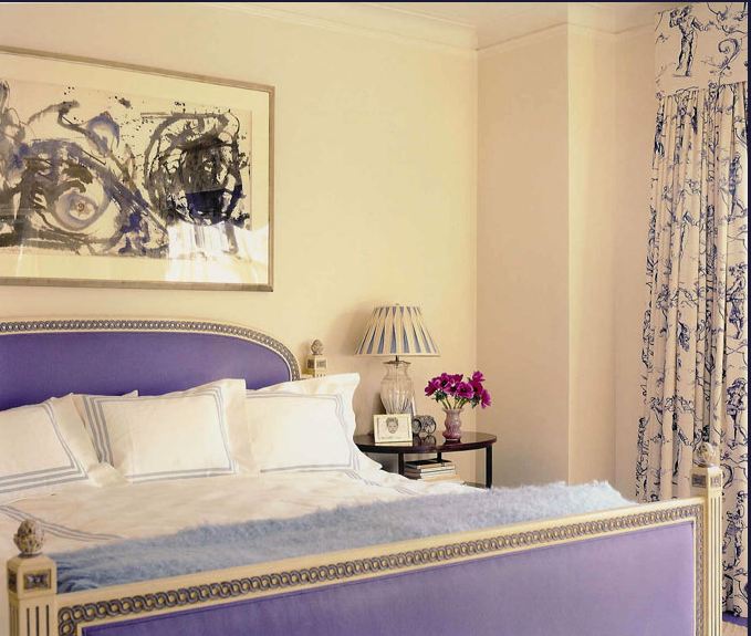 Bedroom with white bedframe with purple upholstered head and foot board with link detail trim, white bedding with blue embroidery, a fuzzy blue throw, and blue and white curtains