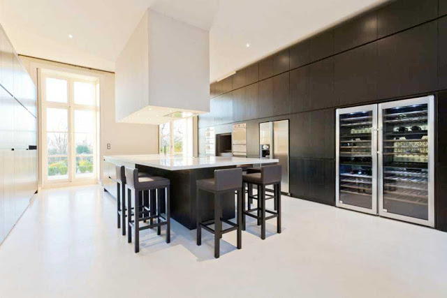 modern kitchen with hidden appliances, black island with white counter top, over sized square pendant light, bar chairs, and two wine cabinets