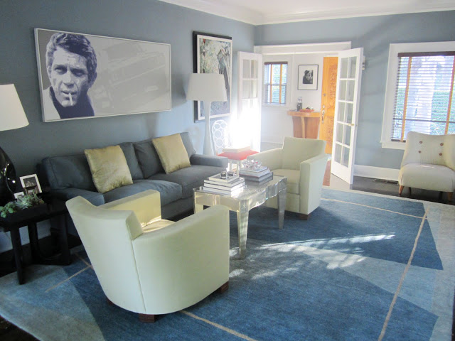 Blue living room with Steve McQueen painting, French doors, large area rug, cream colored arm chairs and a lucite coffee table