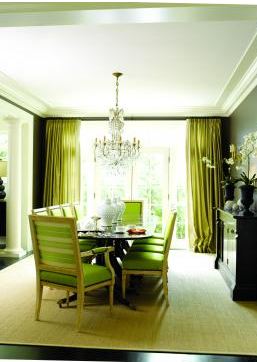 Dinning room with dark brown walls, a dark wood floor, a sea grass area rug, Kelly Wearstler fabric upholstered chairs, a large picture window with green floor length curtains and a crystal chandelier