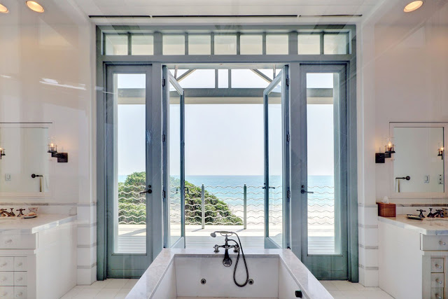 ocean view from the white master bathroom with stand alone bathtub facing blue trimmed glass doors and windows lead onto a balcony.