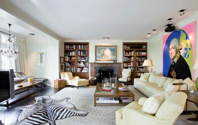 Family room in a mansion with zebra skin rug, wood floor, fireplace, built in bookshelves, white sofa and a large modern art portrait of George Washington