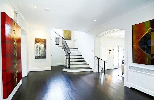 Grand foyer with dark wood floors, stairs with iron railings and large pieces of modern art