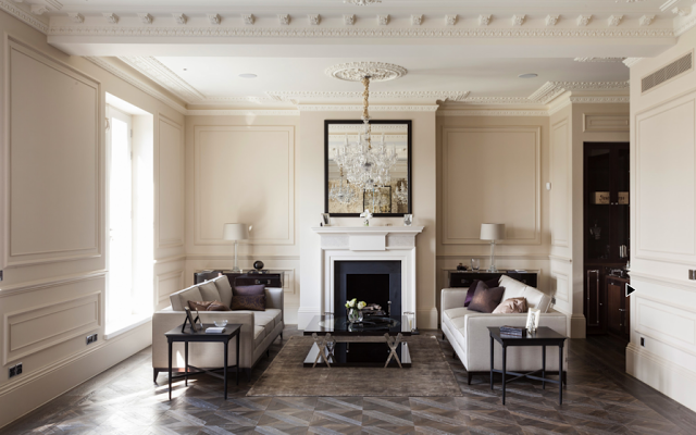 Living room in a suburban London home with carved crown moulding, ceiling medallions, parquet wood floors, decorative wall moulding and paneling and dueling sofas