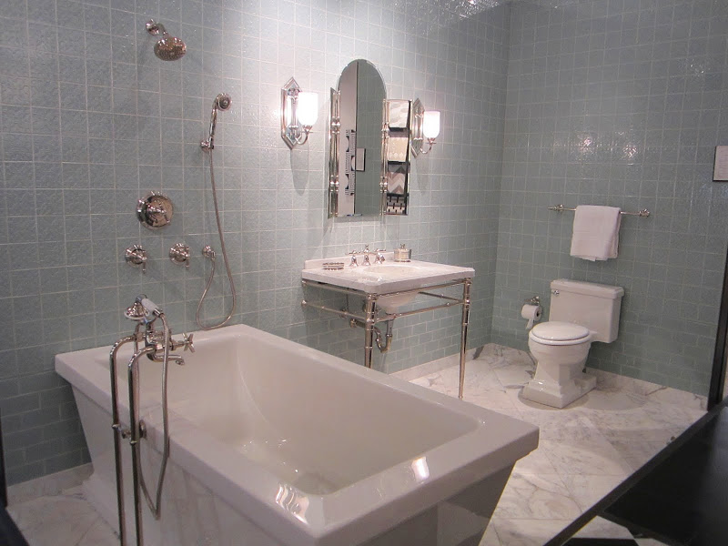 Alternative view of a bathroom with Michael S. Smith's Labyrinth tiles for Ann Sacks from floor to ceiling, an undermount sink where you can see the pipes. a marble tile floor and a freestanding tub