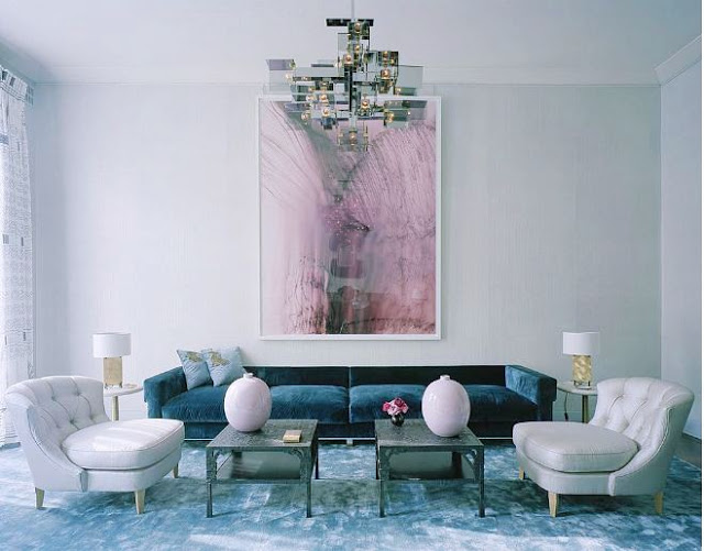 Living room in london with a blue velvet sofa, light grey tufted armchairs, two small coffe tables, a modern chandelier and a pink piece of modern art on the wall