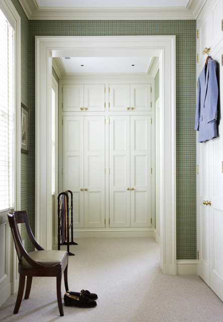 A closet with green plaid wallpaper and white cabinets with gold door pulls