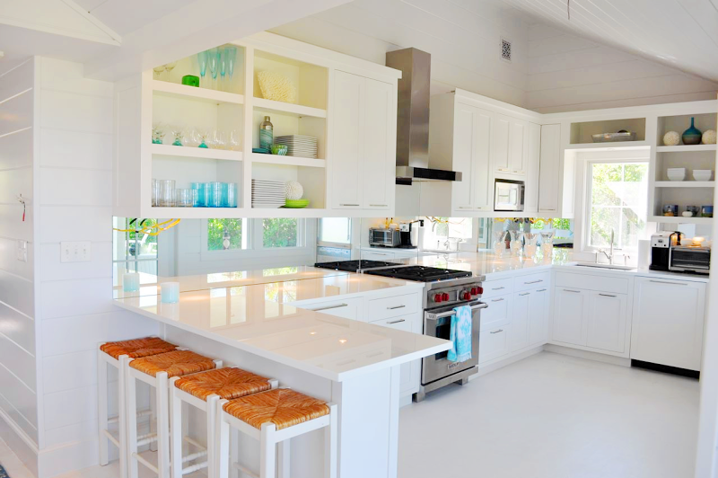 Kitchen with a deluxe Wolf range, near white Caesarstone counters, white cabinetry with long silver drawer pulls and open upper shelving, a white lacquered floor and stainless appliances