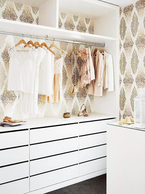 Girly walk in closet with white drawers, a shelf for shoes, hangers and wall paper with gold diamond filigree pattern