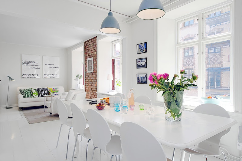 View of the white living room and dining room with blue pendant lights, large windows, white table and chairs