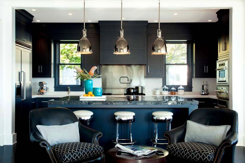 Kitchen with dark blue cabinets, white backsplash, black and white barstools at a dark blue island, stainless appliances and three silver pendant lights