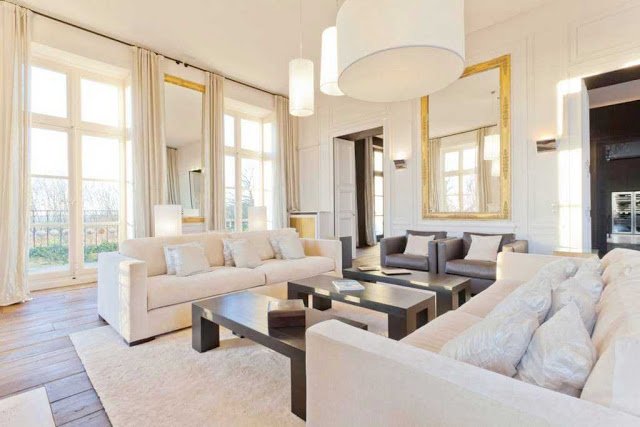 living room with white dueling sofas, french doors, three rectangular coffee tables, wood floors, pendant lights and a large mirror with a gold frame