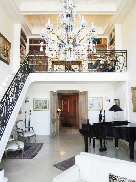 Grand staircase to the second level of a Paris apartment with a chandelier, grand piano and louis chairs