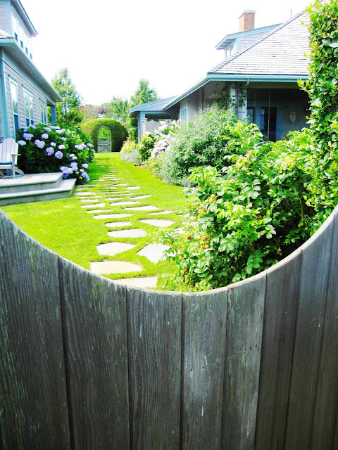 View of a stone walkway in a backyard in Nantucket from over a wooden fence