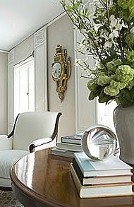 Close up of round wood table in a grey bedroom with a white armchair, crystal ball, flower arrangement and a gold clock