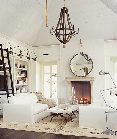 living room with dueling sofas, a marble top coffee table separating them, a fireplace with a round mirror on the mantel, metal chandelier, built in bookcase and cabinets with a sliding ladder to reach higher shelves