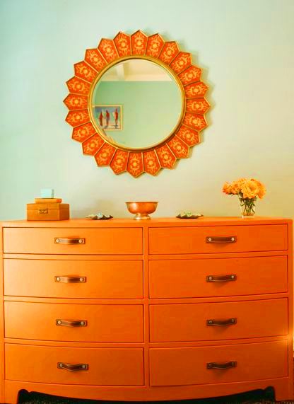 Orange chest of drawers under and orange sunburst mirror