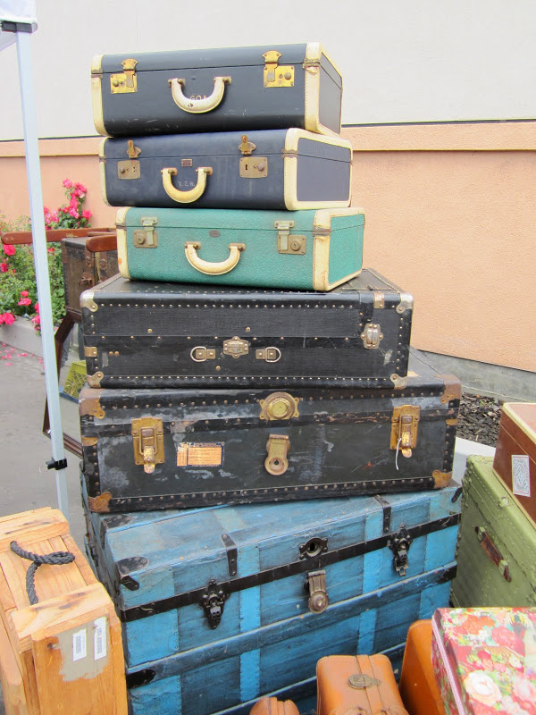 Stack of three vintage suitcases on two black chests on top of a blue steamer trunk