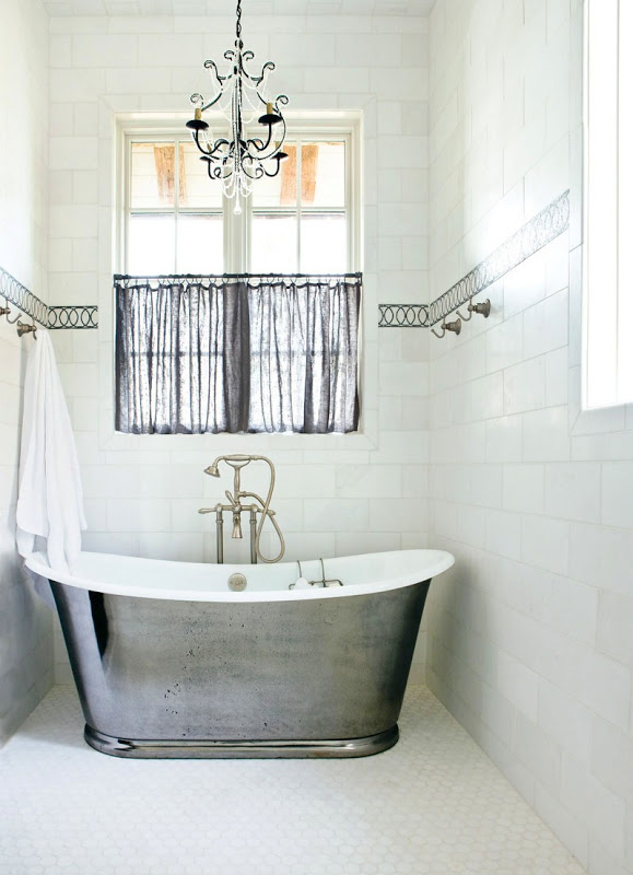 Bathroom with tile walls and an accent stripe, a window with sheer black curtains, a chandelier and a silver stand alone bathtub
