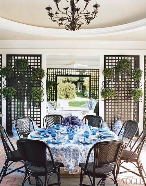 tory burch home estate with trellis garden structures, table cloth on a round table, bistro chairs, blue floral table cloth