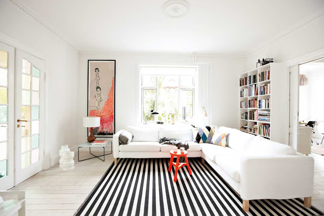 living room modern orange accents, black and white striped rug, white sectional sofa, white bookcase full of books and french doors