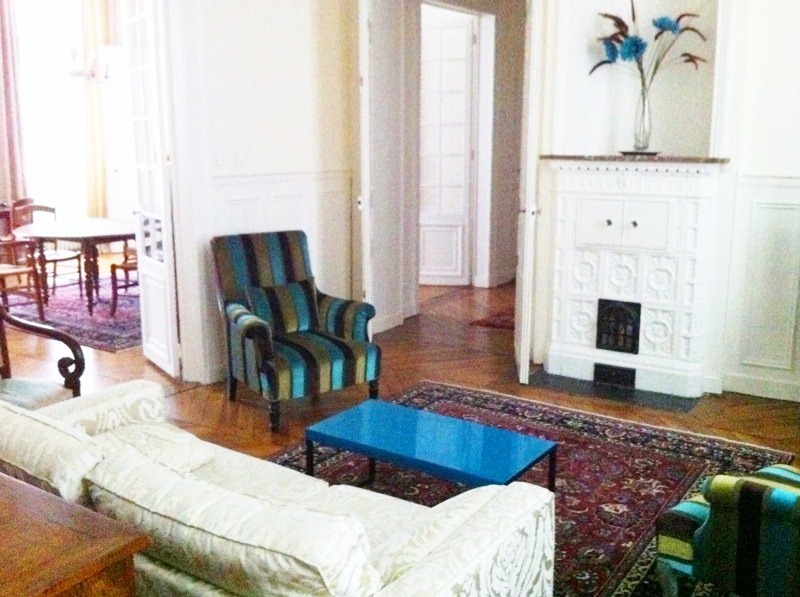 Family room in a Paris apartment with herringbone wood floor, white sofa, striped blue, green and black armchairs, a blue coffee table and a Turkish rug