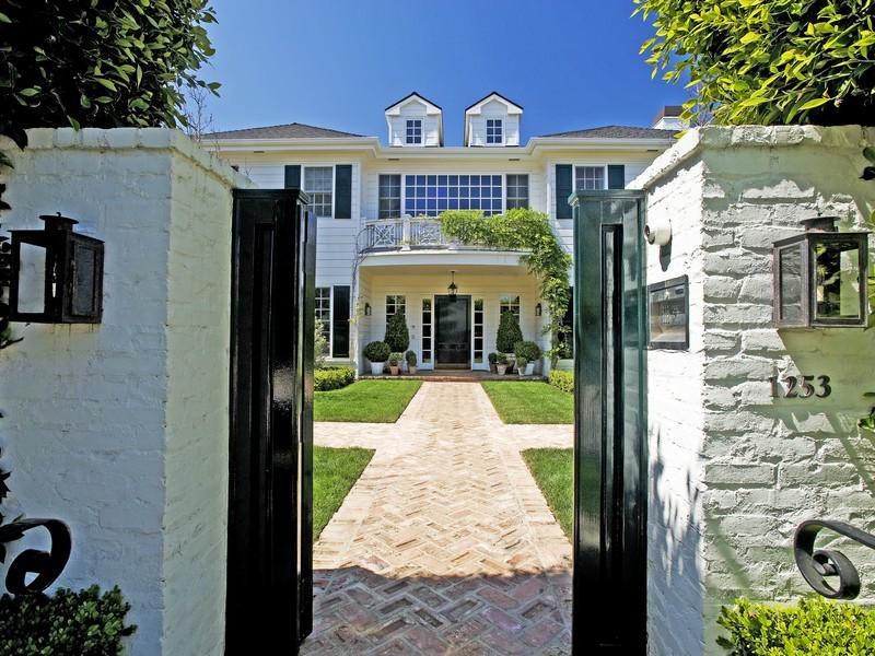 Painted white walls with a black gate open to a herringbone brick walkway up to a white colonial style home in the Pacific Palisades