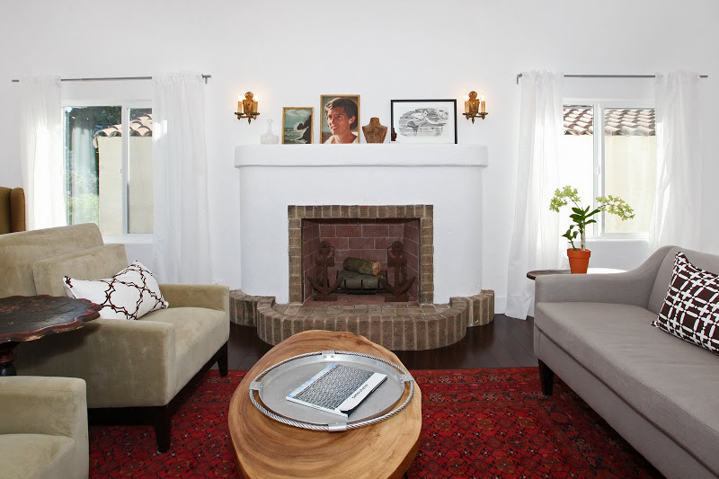 Living room in a Spanish Style home with Koa wood floor, wing back armchairs and a grey sofa with COCOCOZY decorative throws and pillows, red Moroccan rug and brick fireplace