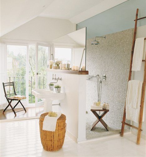 Bathroom with white painted wood floors, double french doors leading to a small patio, a shower open on both sides with one wall doubling as a backsplash for the pedestal sink and pebble mosaic on the walls and floor