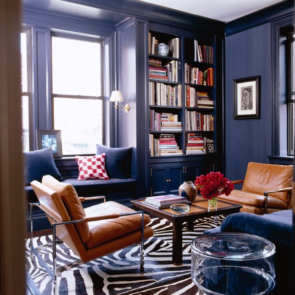 Library with blue walls, leather armchairs, a coffee table with inlaid wood details, a zebra print rug, a window seat and built in bookshelves full of books
