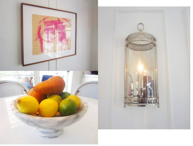 kitchen finishing touches: a polished nickel silver sconce light, marble fruit bowl holding lemons, limes and pears, and a framed piece of a child's art