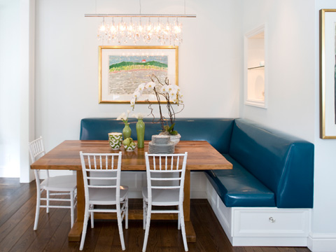 kendall wilkinson' breakfast nook with a large wooden table surrounded by white chairs and benches with blue leather coverings