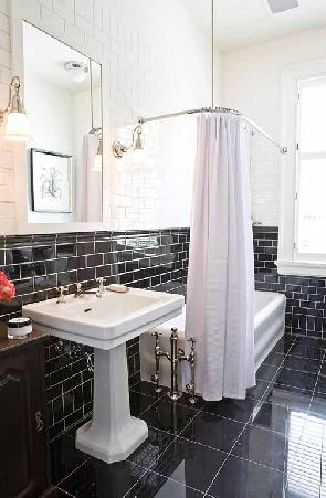 mcintyre bills' black white bathroom bath with black tiles on the floor, black and white subway tiles on the walls, a white freestanding tub with white shower curtain and a white pedestal sink