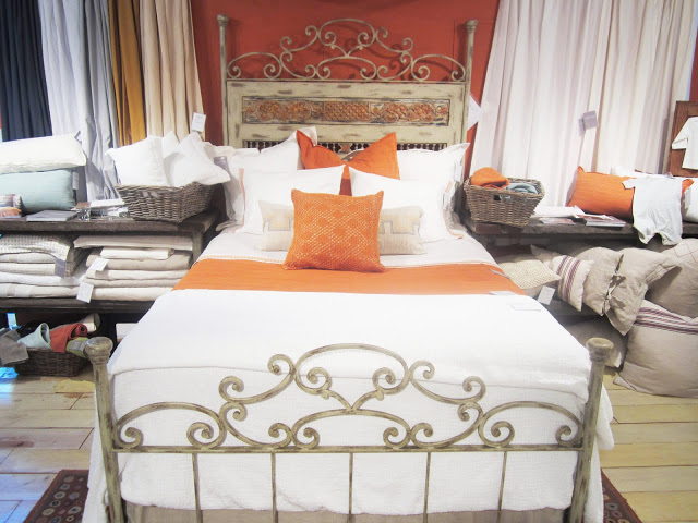 Pumpkin and white bedding by Coyuchi on a bed with a metal frame with a painted headboard and art deco details on the head and foot boards