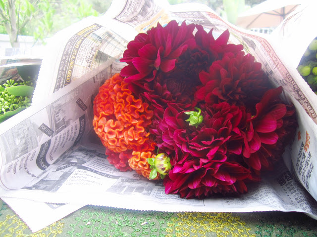 bouquet of dahlias and coscums wrapped in newspaper on a deck table