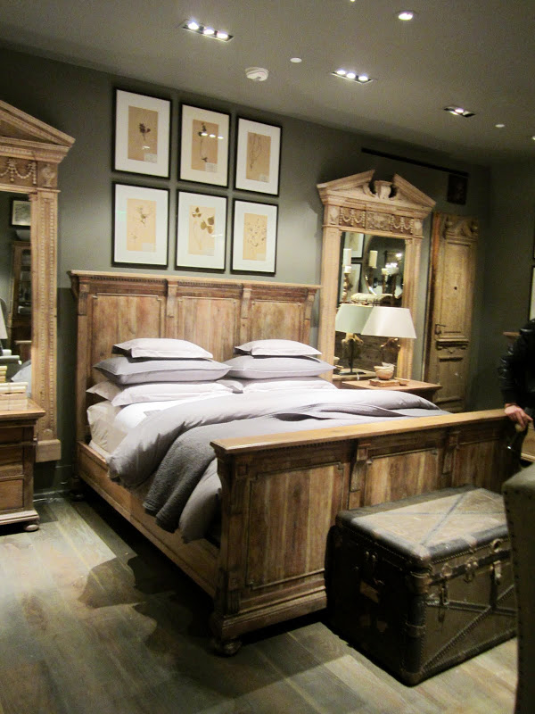 Bedroom in Restoration Hardware with a wood bed frame, chest at the foot of the bed, two large mirrors in antique wood frames