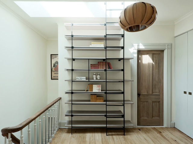 Gray floating shelves with a black ladder going up to a skylight 