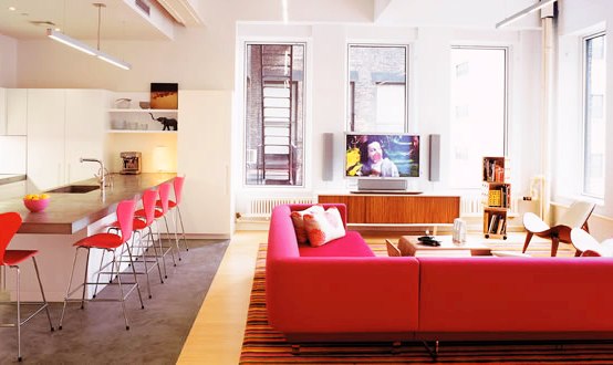 Open plan kitchen and living room with bright pink sofa and bar stools in a modern New York loft