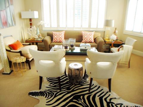 Living room in Ron van Empel of Empel Collections' home with zebra print rug, silver Chinese garden stool, white armchairs and a taupe sofa with orange and white graphic print accent pillows