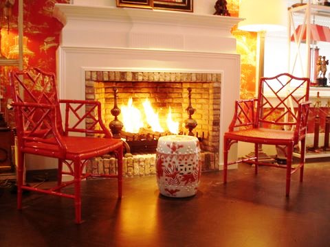 Ron van Empel of Empel Collections' home showroom with Red chinoiserie toile wallpaper around a white fireplace with two coral faux bamboo Chippendale chairs and a red and white Chinese garden stool