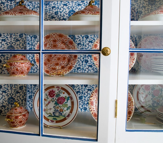 Glass front upper kitchen cabinets with blue and white wallpaper inside the cabinets