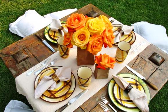 Outdoor picnic table with plaid enamel plates and cups, a simple white runner and an original centerpiece made of gorgeous orange roses in brown paper bags by Lily Lodge