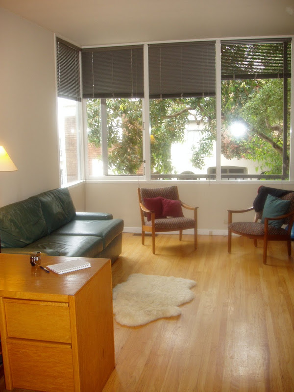 Living room before Niche Interiors's redesign with green leather sofa, dark blinds, midcentury modern chairs and a teacher's desk
