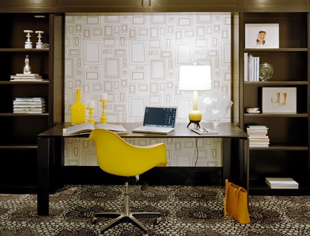 Dark brown home office with built in shelves and cabinets, graphic wallpaper and a yellow Eames chair at a desk
