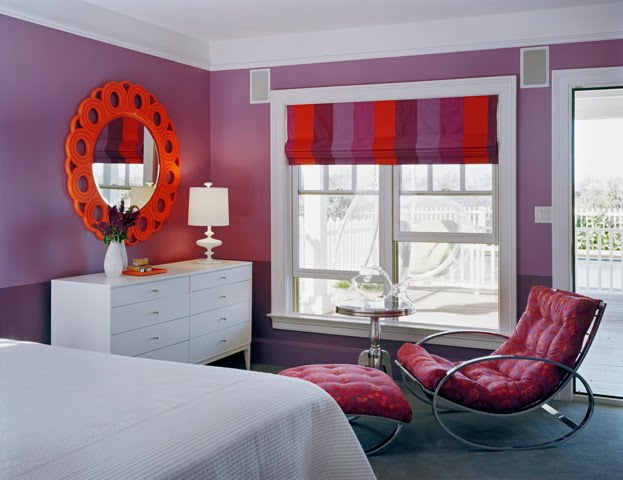 Purple bedroom by Ghislaine Vinas with white dresser, orange mirror, chaise lounge and purple and orange striped Roman shades
