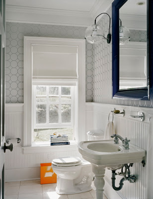 Bathroom by Ghislaine Vinas with wainscoting on the walls, grey wallpaper and a porcelain washstand and bright orange wastebasket