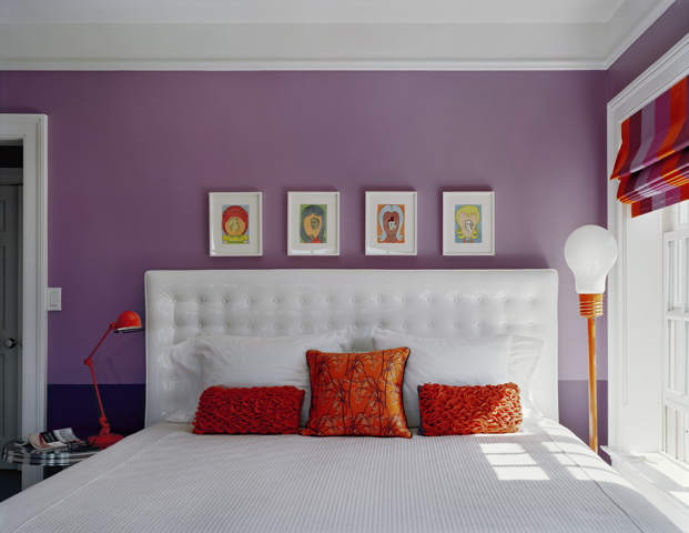 Purple bedroom by Ghislaine Vinas with a white tufted headboard with orange accent pillows and lamps