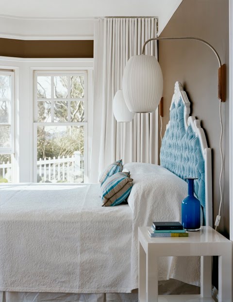 Turquoise and brown master bedroom by Ghislaine Vinas with a light blue tufted headboard with white trim and a modern white side table 