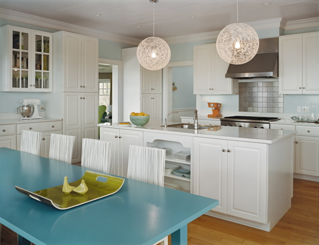 Eat in kitchen by Ghislaine Vinas with white cabinets, stainless steel square tile backsplash, round pendant lights, light blue walls and a long turquoise dining table surrounded by modern white chairs