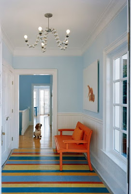 Light blue entryway by Ghislaine Vinas with a bright orange bench and striped rug